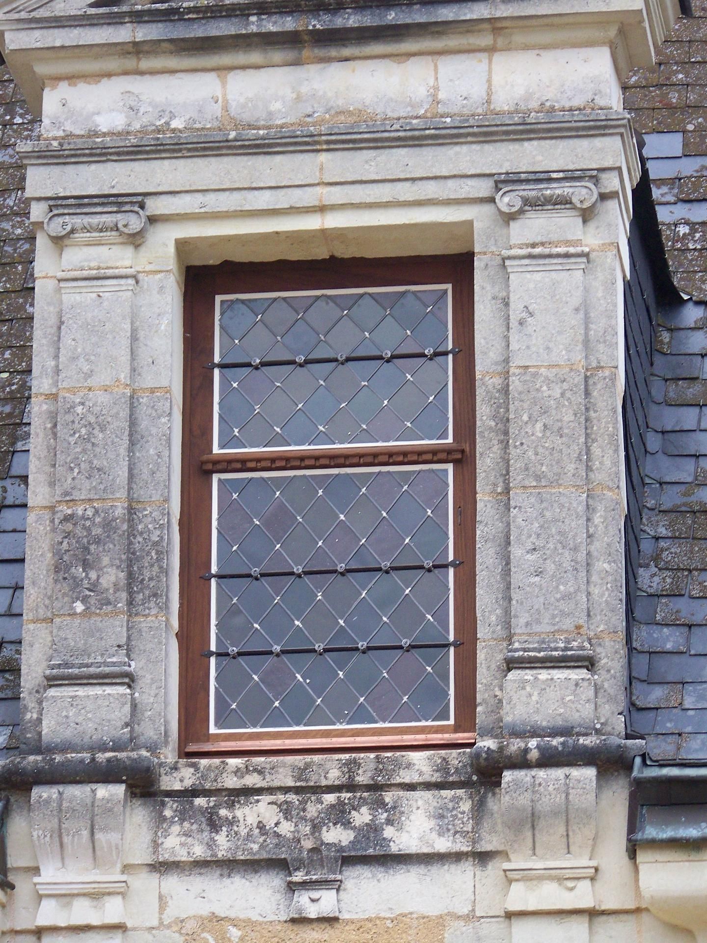 Fenêtre à carreaux en losanges, encadrée de pierre sur un toit d'ardoise.