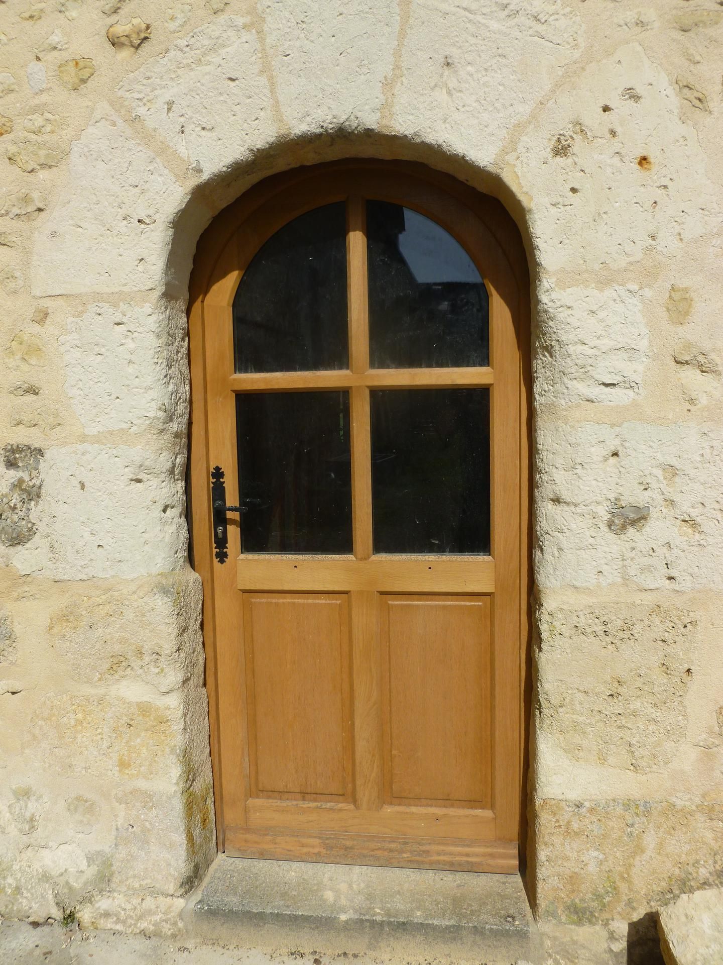 Porte en bois avec fenêtre cintrée dans un bâtiment en pierre.