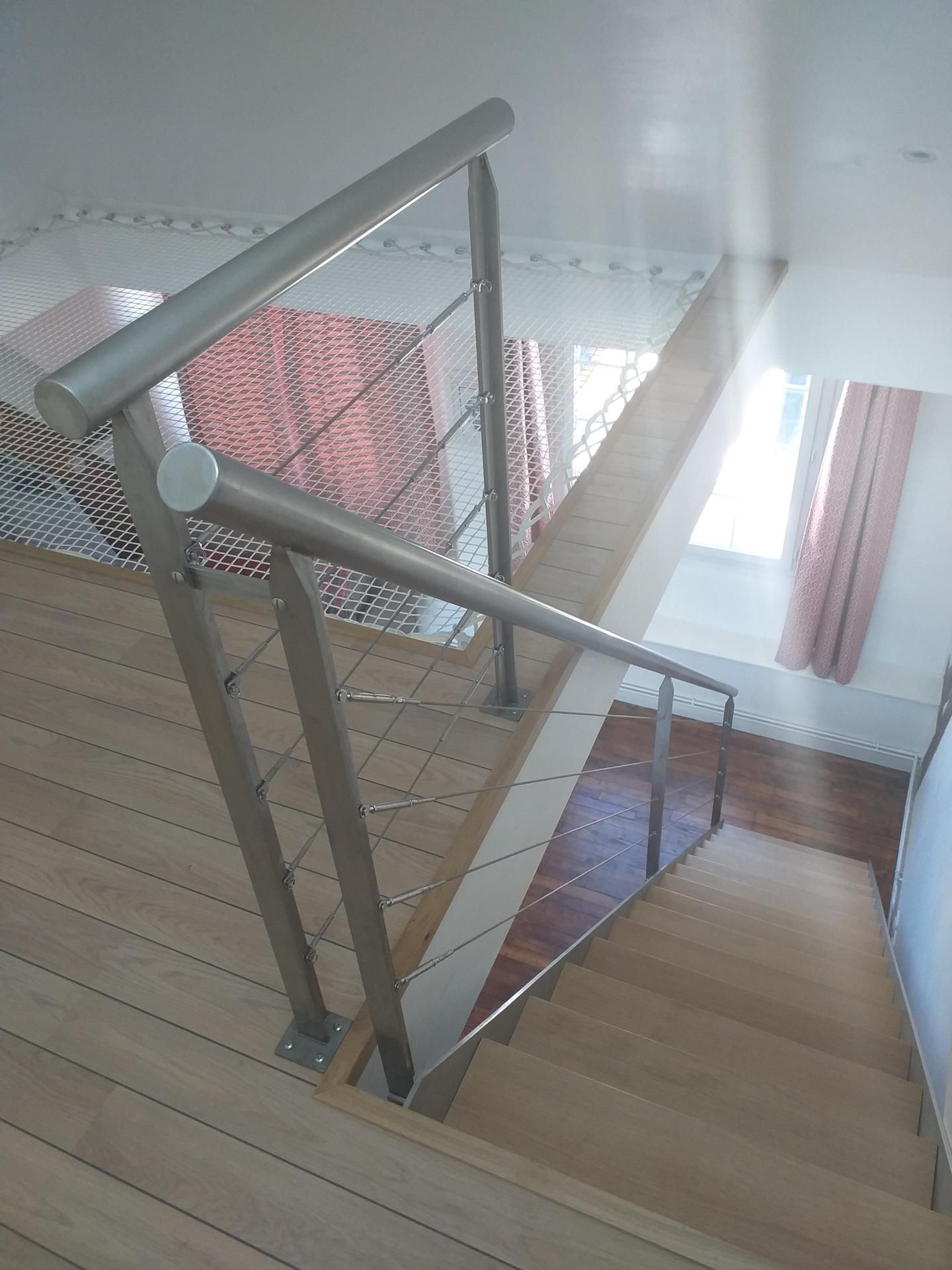 Escalier en bois avec une rampe en métal. La lumière du soleil inonde la pièce par une fenêtre.