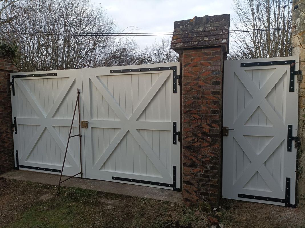Portail en bois blanc orné d'un motif en « X », quincaillerie noire et pilier en briques.
