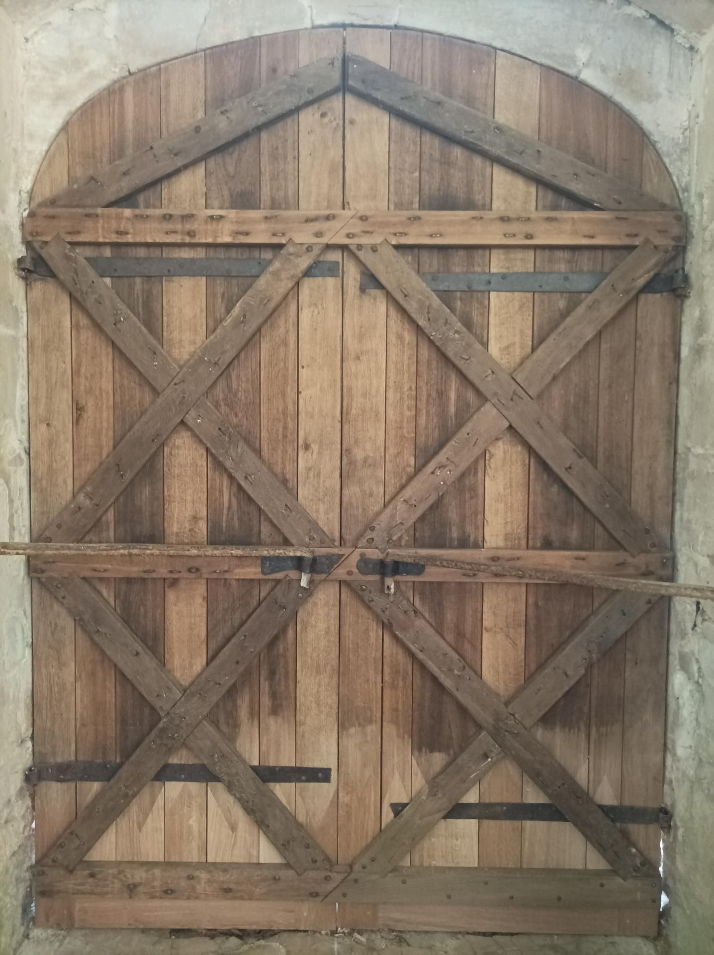 Porte cintrée en bois avec renforts diagonaux et quincaillerie métallique.