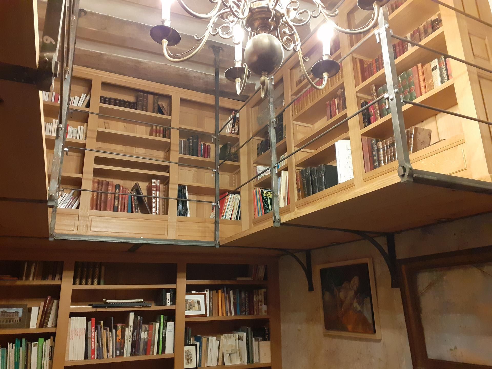 Des étagères en bois avec une mezzanine, éclairées par un lustre. Les étagères sont remplies de livres.