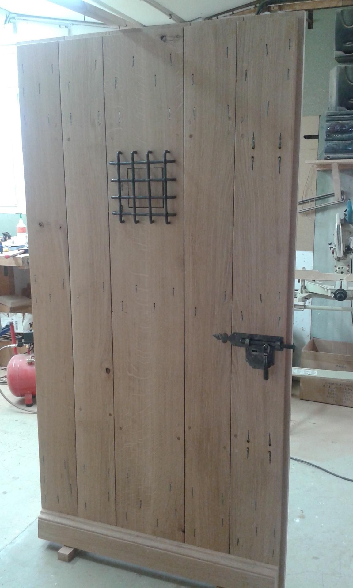 Porte en bois avec grille et loquet en métal, aspect vieilli, pour usage intérieur.