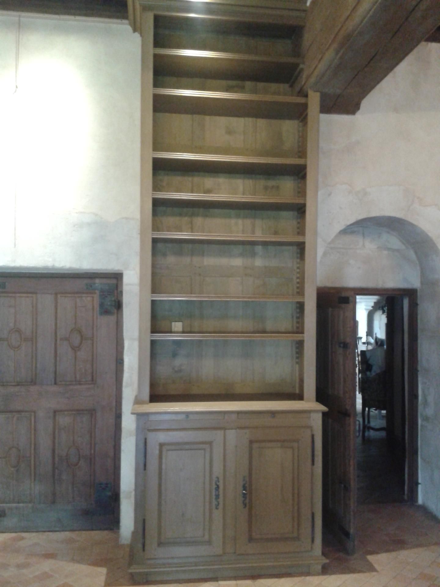 Haute bibliothèque en bois avec portes d'armoire ; à l'intérieur d'une pièce avec une porte cintrée et une porte en bois.