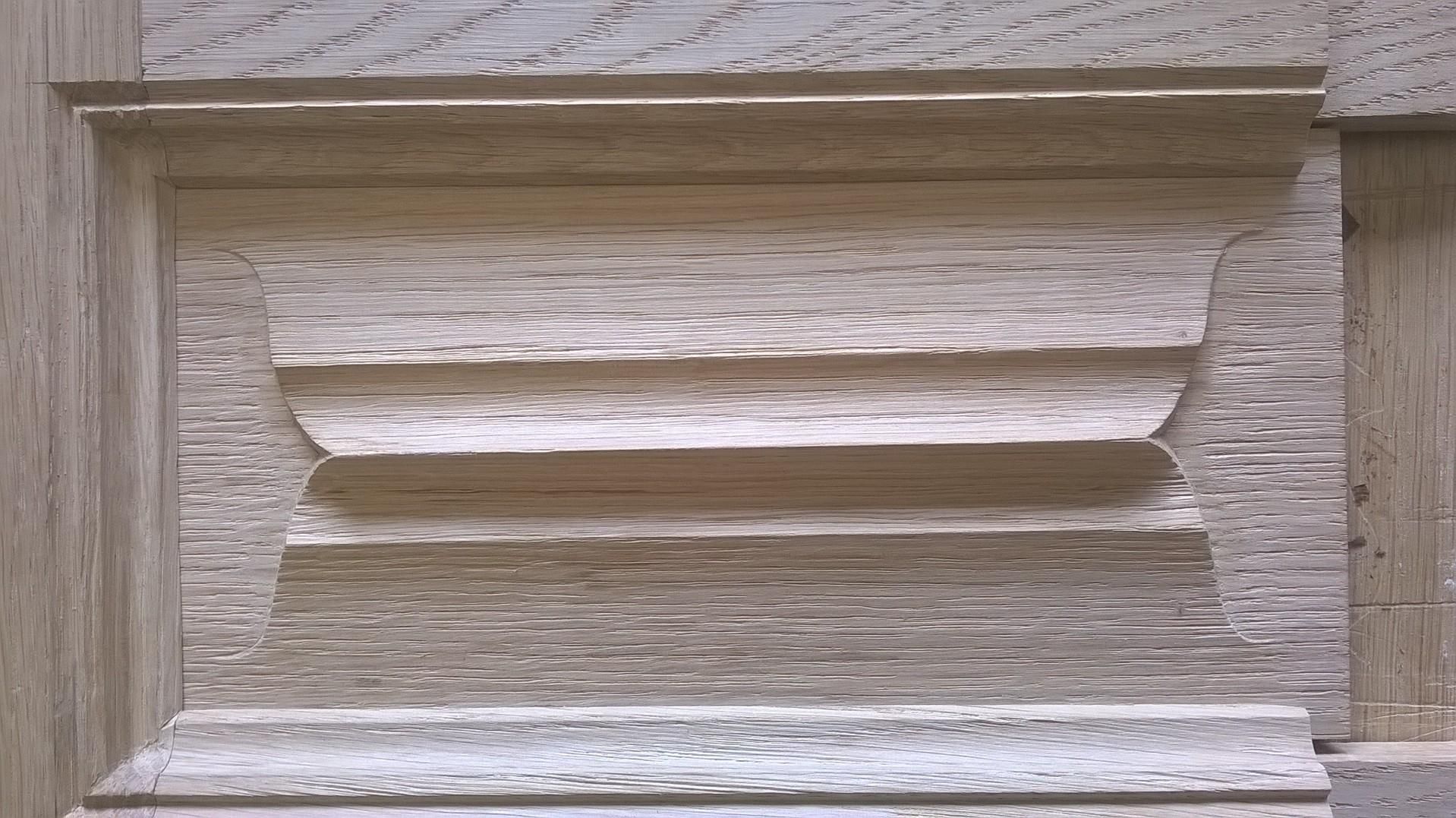 Gros plan sur un panneau de bois sculpté présentant des éléments décoratifs rectangulaires et courbes superposés.