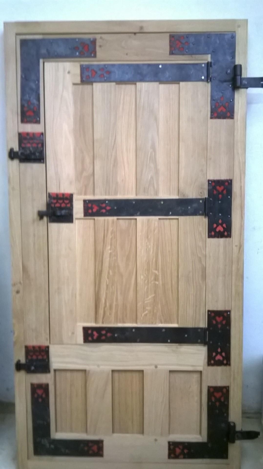 Porte en bois avec charnières en métal noir et accents décoratifs rouges.
