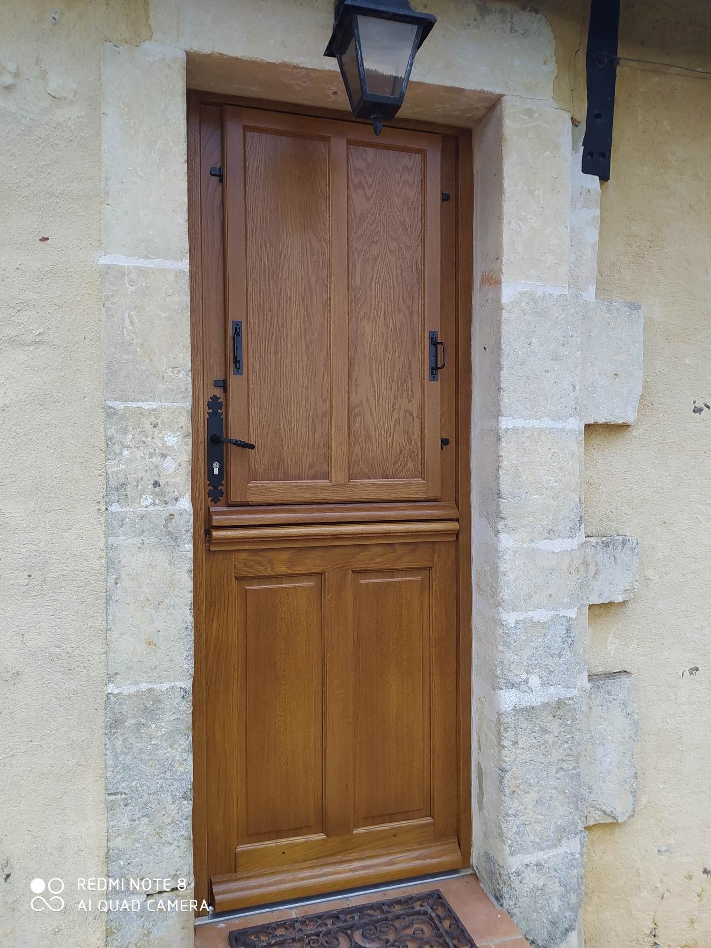 Porte hollandaise en bois avec quincaillerie noire, encadrée de pierre et surmontée d'une lanterne.