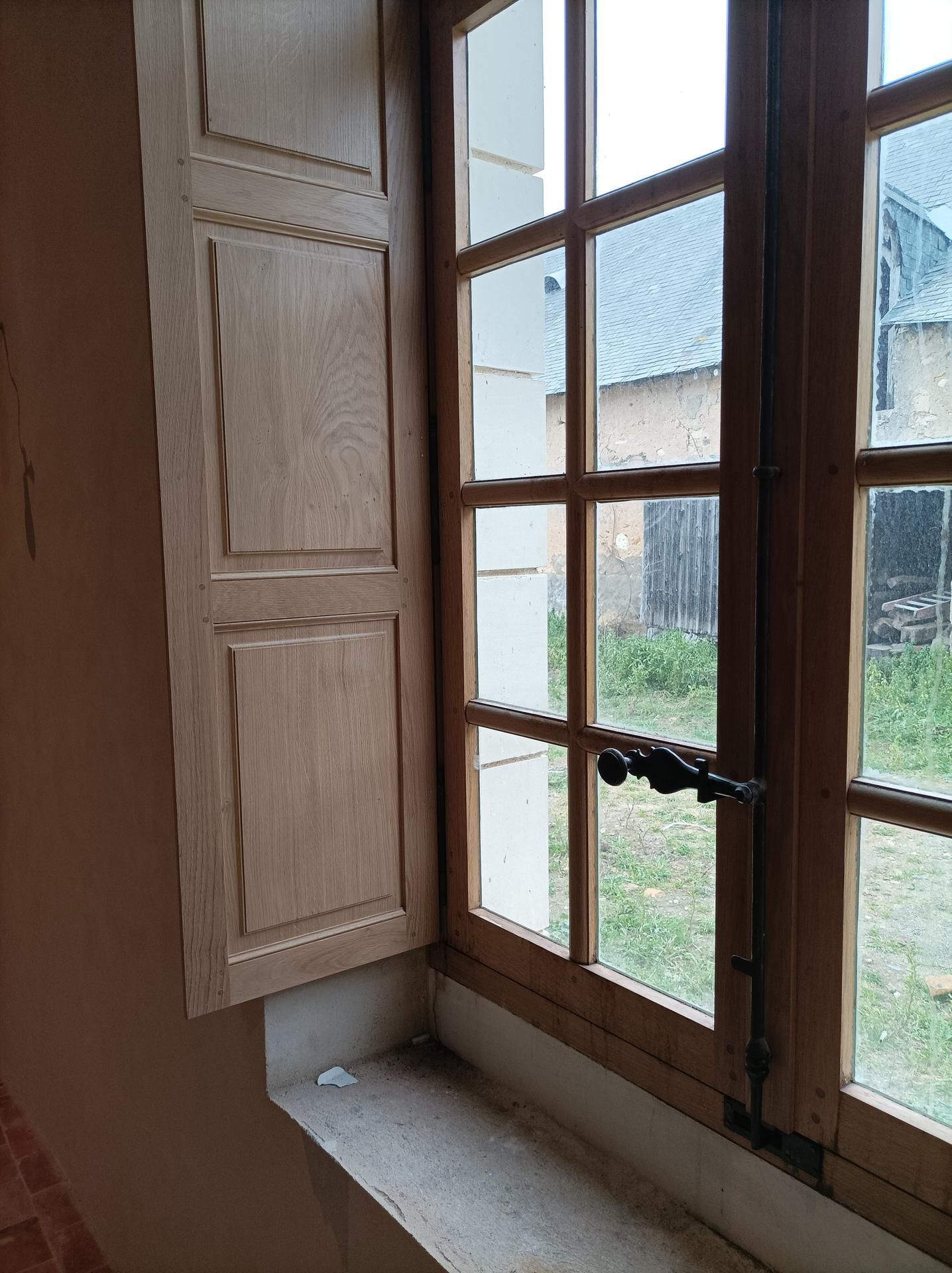 Fenêtre en bois avec un volet ouvert. Vue extérieure sur la pelouse et le bâtiment.