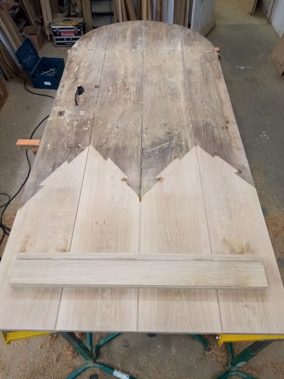 Table en bois en cours de fabrication, avec des pièces découpées disposées dessus ; présence de sciure.