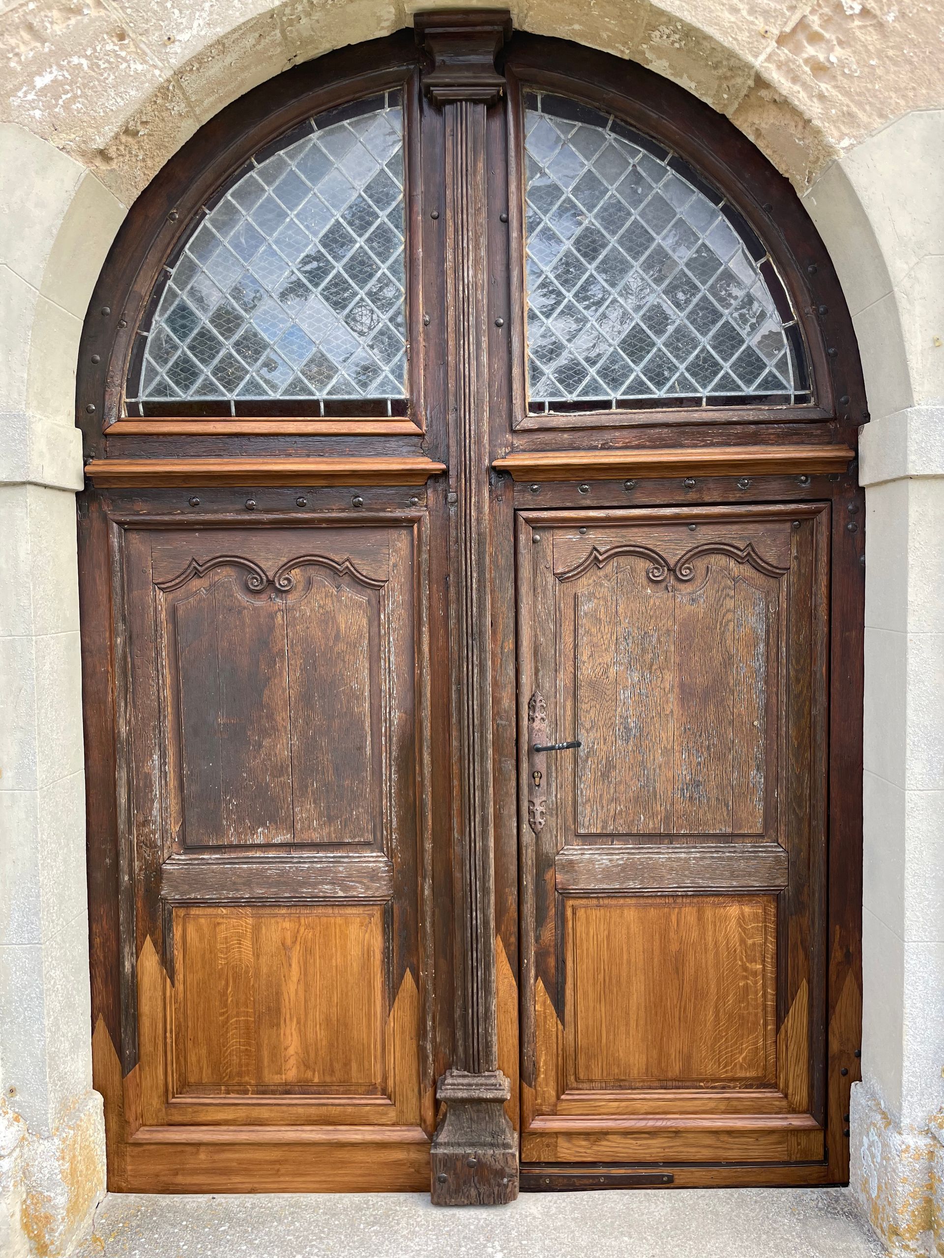 Vieilles portes doubles en bois avec une fenêtre cintrée en partie supérieure, présentant des signes d'usure.
