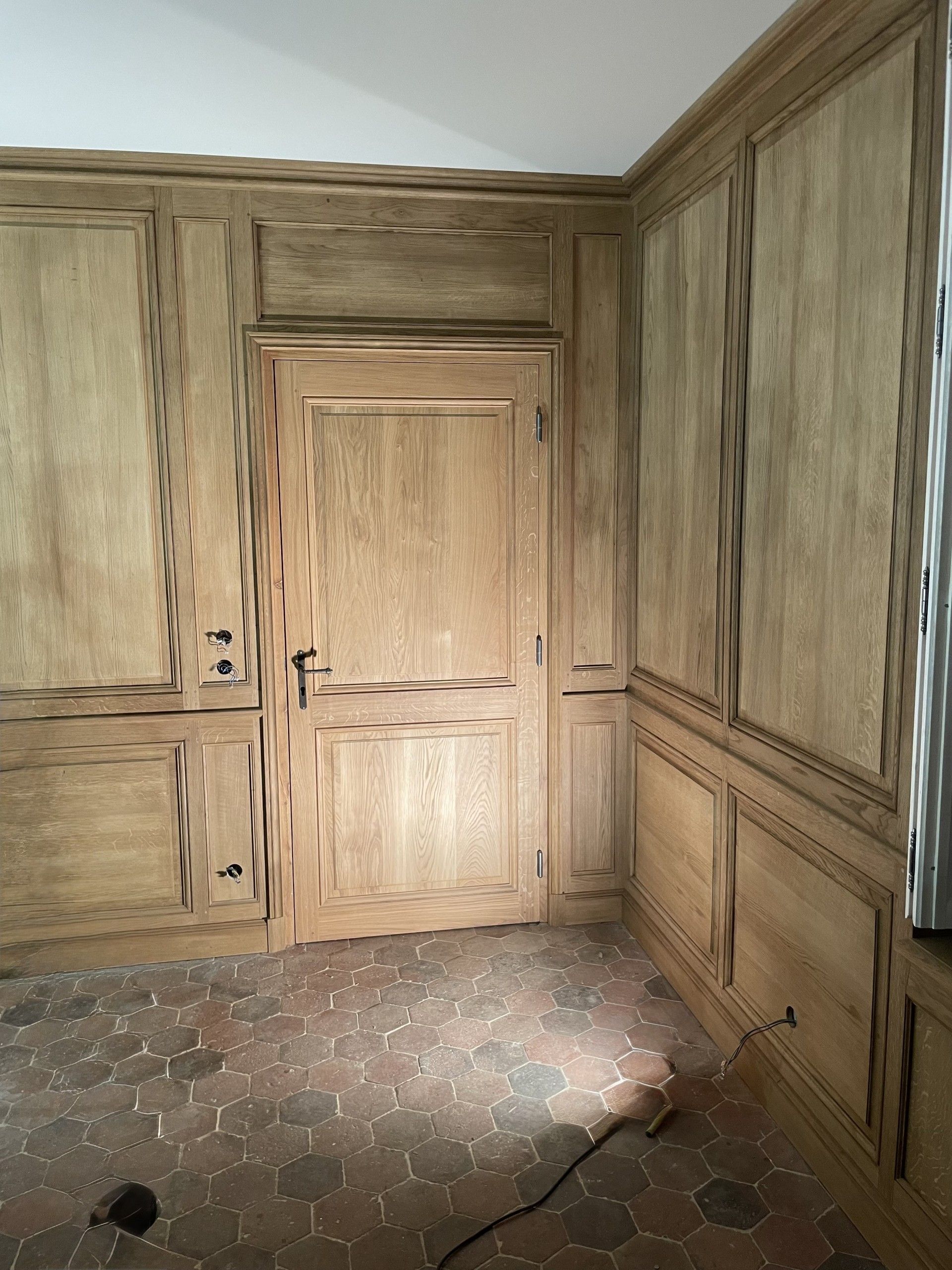 Lambris avec une porte dans une pièce au sol carrelé en terre cuite.