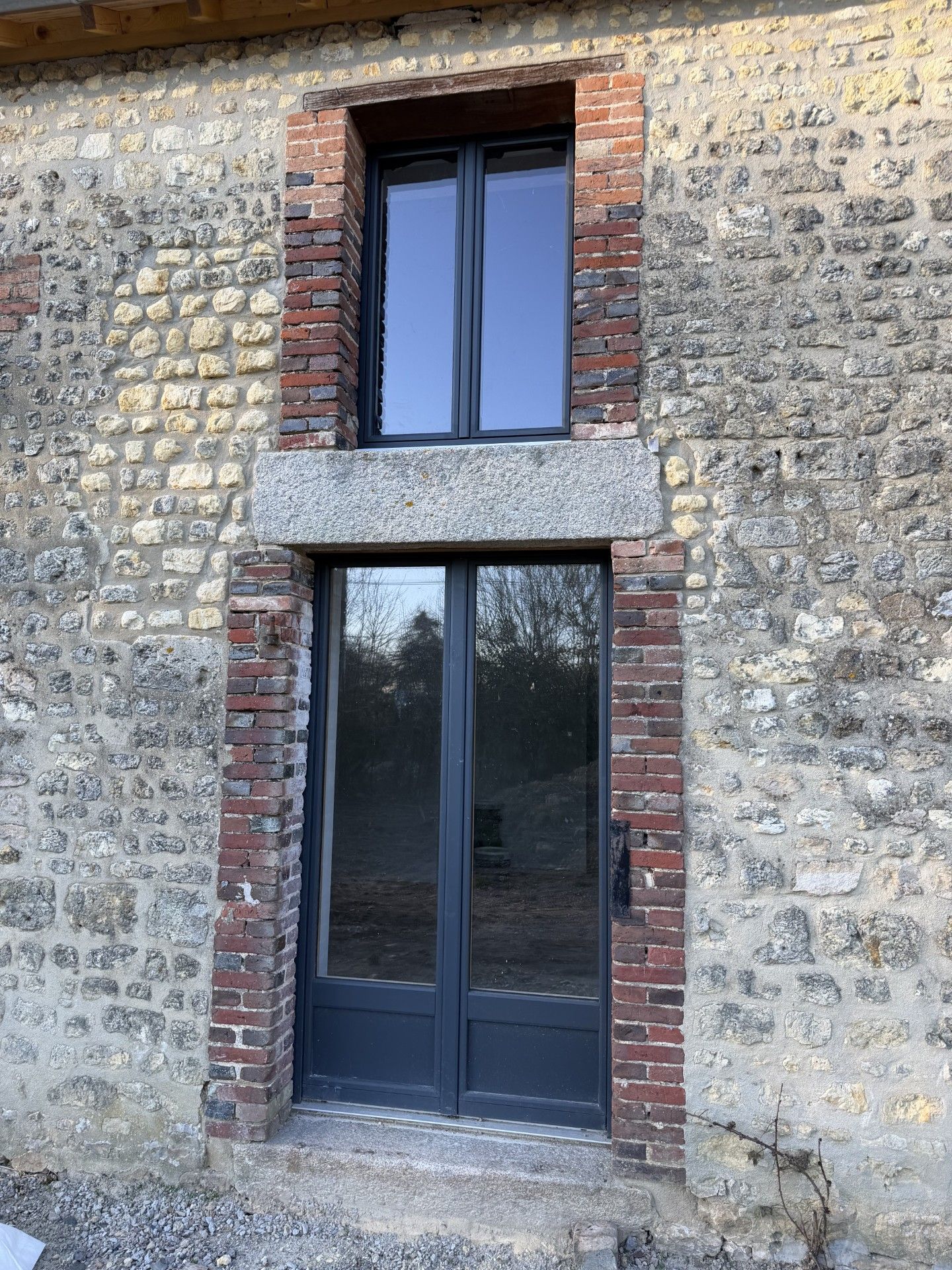 Extérieur d'un bâtiment à façade de briques et de pierres ; porte et fenêtre à encadrements sombres.
