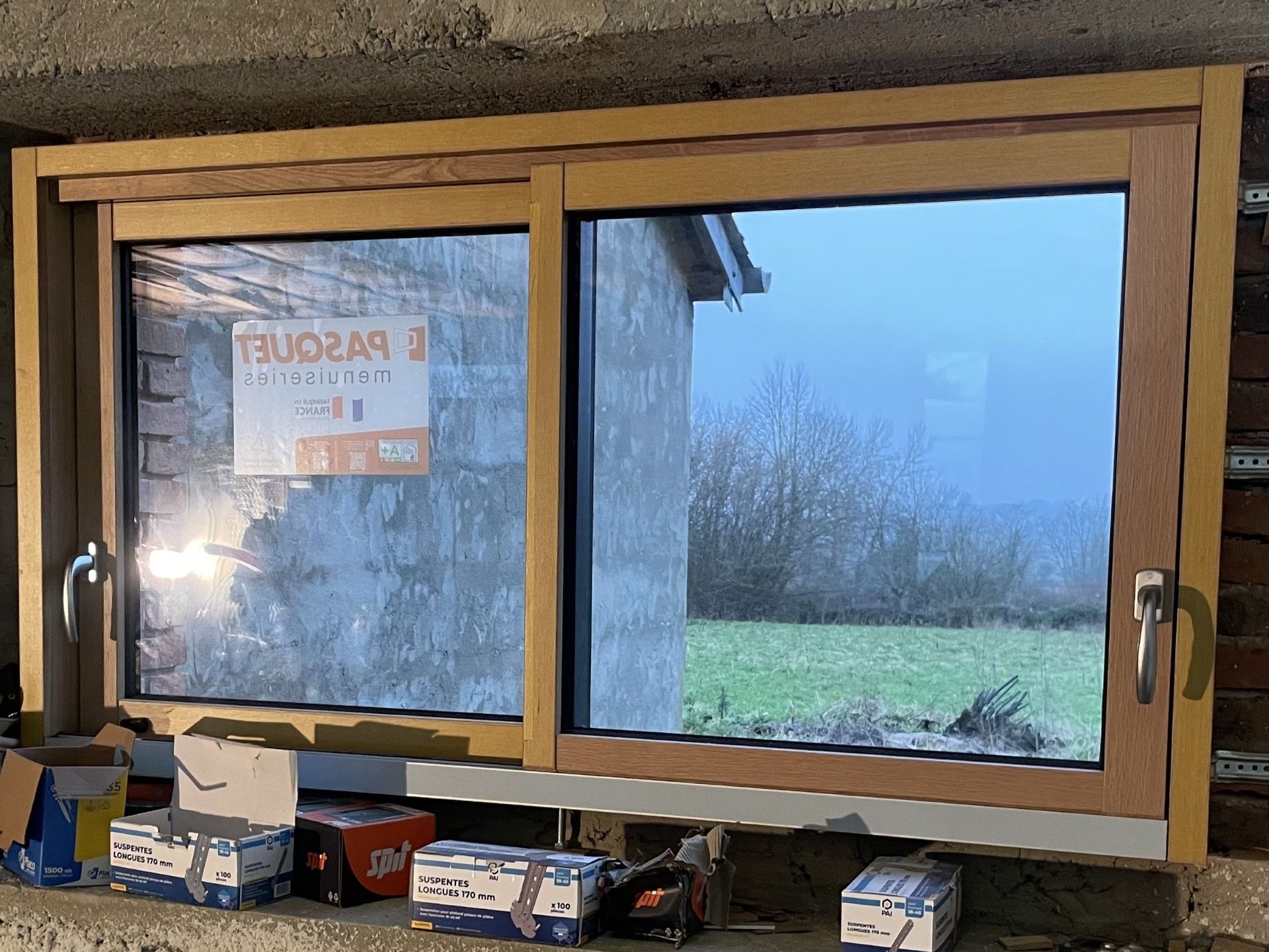 Fenêtre coulissante à cadre en bois installée dans un mur en béton, reflétant un paysage extérieur brumeux.