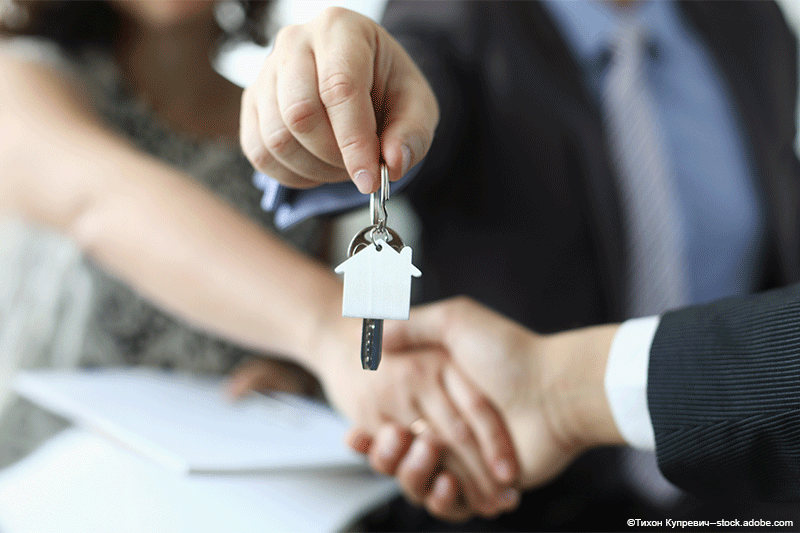 Eine Person im Anzug überreicht einer anderen Person per Handschlag die Hausschlüssel.