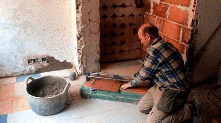 Un hombre está arrodillado en una habitación mientras trabaja en un piso de baldosas.