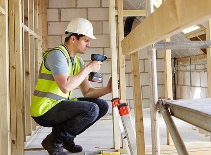 Un trabajador de la construcción se arrodilla mientras utiliza un taladro en una estructura de madera.
