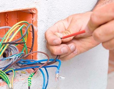 Una persona está trabajando en una pared con cables y un destornillador.