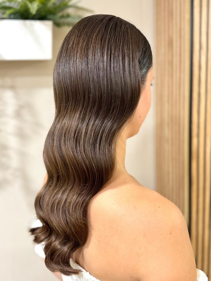 Mujer con cabello oscuro, ondulado y estilo vintage; retrato desde los hombros.