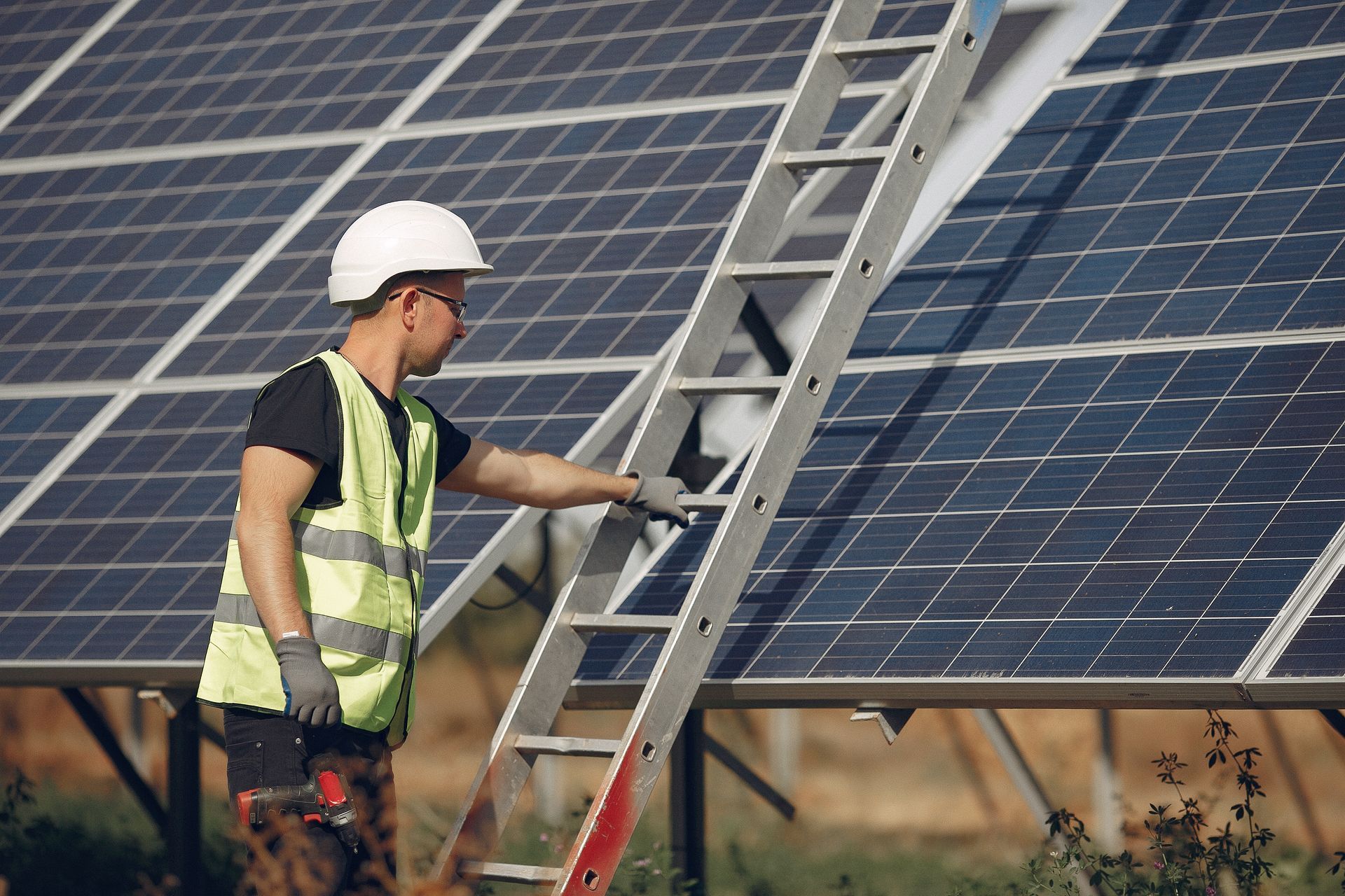 Persona con equipo de seguridad inspeccionando paneles solares mientras está parada en una escalera.