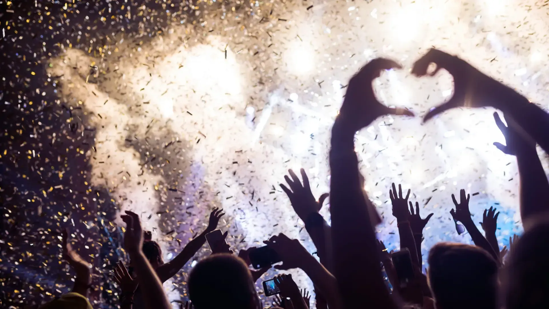 Público en un concierto con las manos en alto bajo las brillantes luces del escenario, confeti