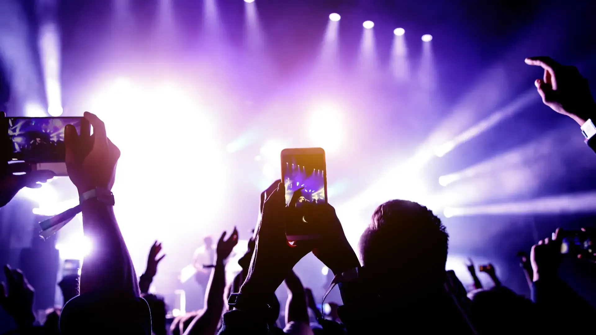 Público en un concierto con las manos y los teléfonos en alto, luces de escenario de color púrpura brillante