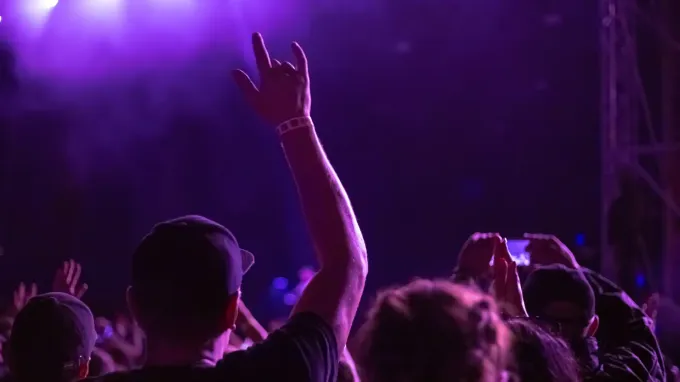 Público en un concierto levantando las manos bajo luces moradas del escenario.