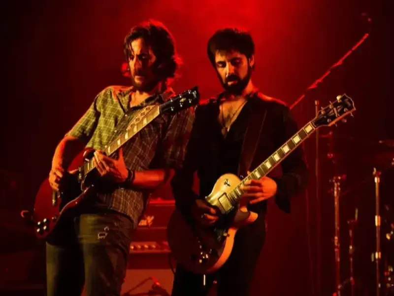 Dos músicos tocando guitarras eléctricas en un escenario iluminado con luz roja.