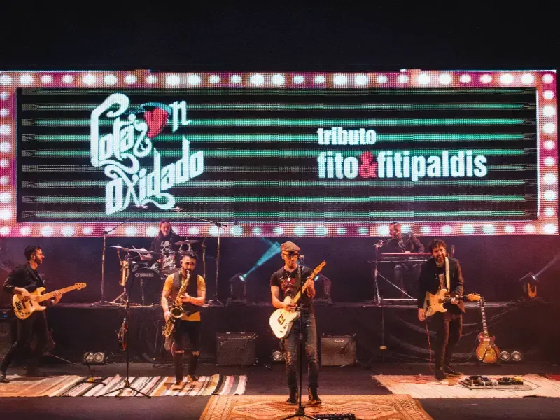Grupo de rock actuando en el escenario bajo un gran letrero LED que dice “tributo fito & fitipaldis”.