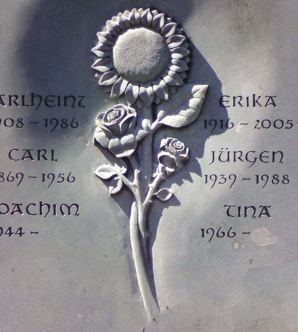 Ein Grabstein mit einer Sonnenblume und Rosen darauf