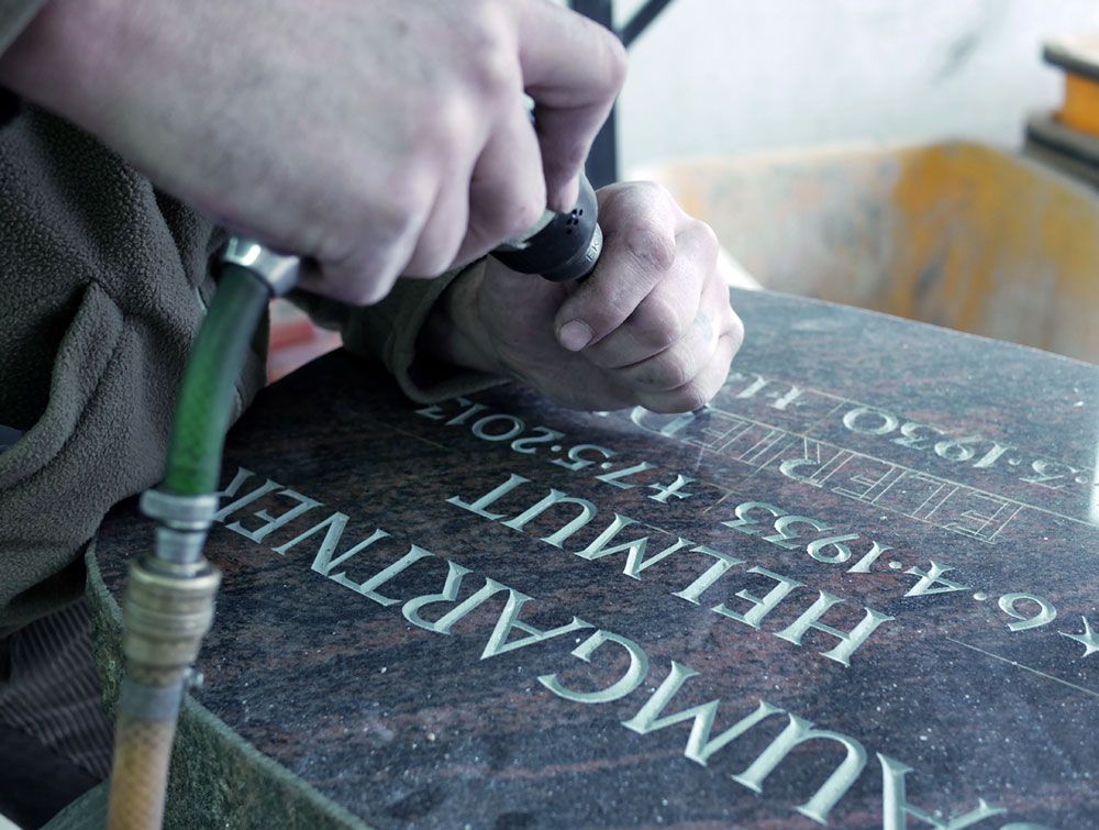 Eine Person meißelt den Namen Helmut in einen Stein