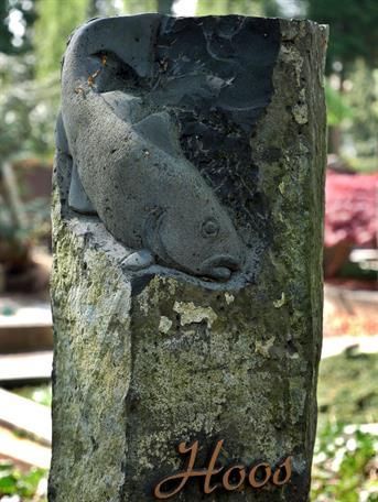 Auf einem Friedhof ist die Statue eines Fisches in einen Felsen gehauen.