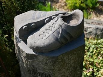 Auf einem Steinblock sitzt eine Schuhstatue.