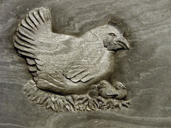 Ein Huhn und zwei Küken sind in eine Steinmauer geschnitzt.