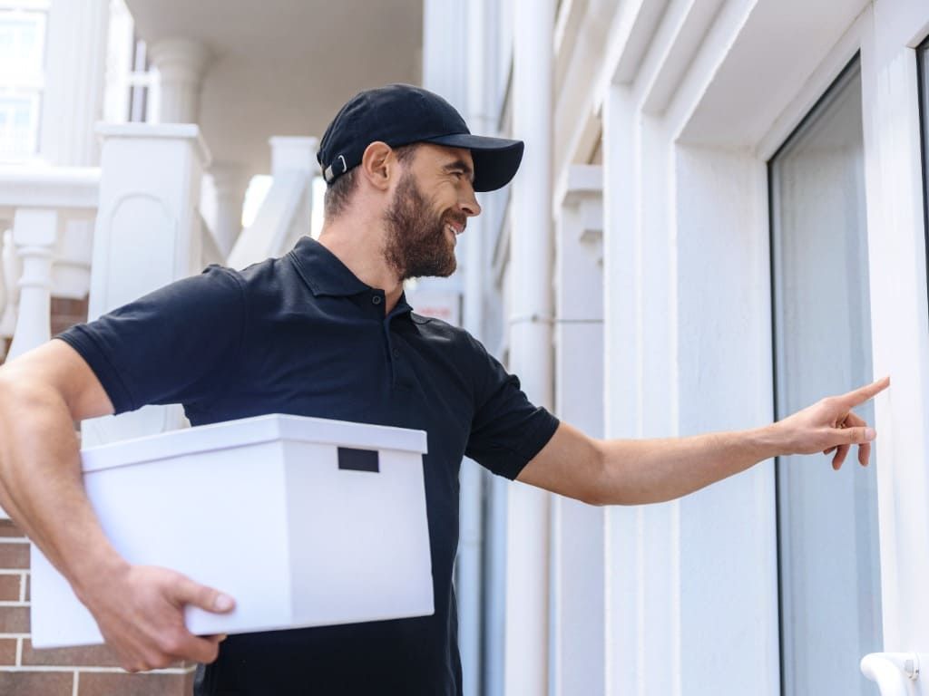 Un repartidor sostiene una caja y señala una puerta.