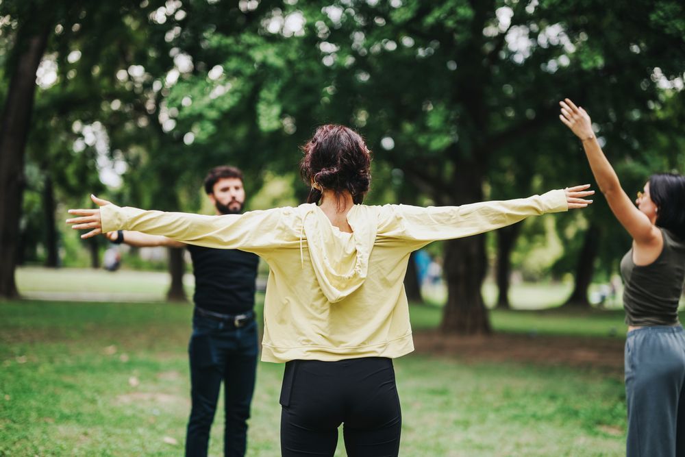 Un grupo de personas estira los brazos en un parque.