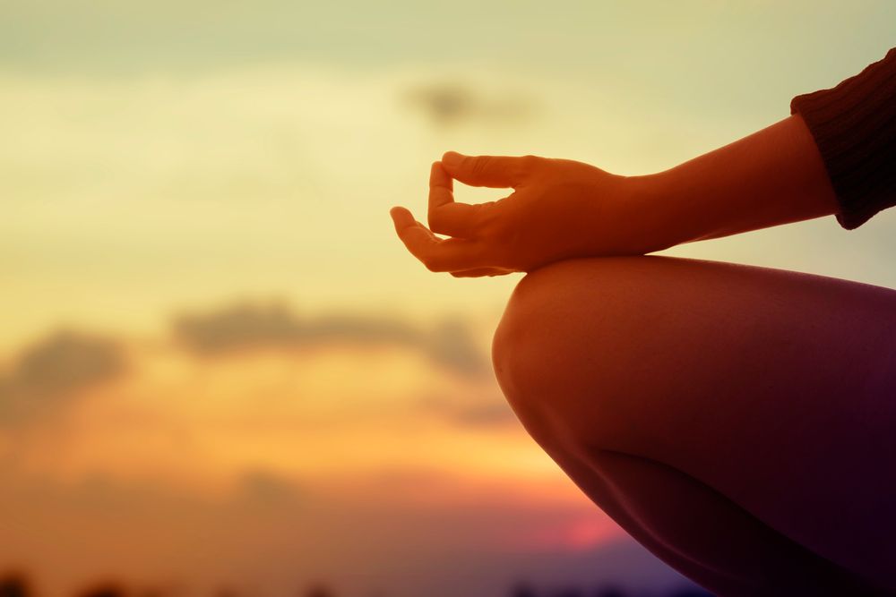 Una persona está sentada en posición de loto con las piernas cruzadas al atardecer.