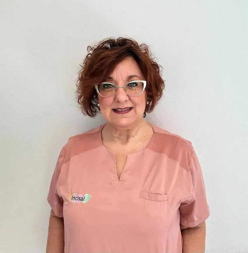 Una mujer que lleva gafas y una blusa rosa está parada frente a una pared blanca.
