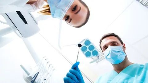 Un dentista y una enfermera miran los dientes de un paciente.