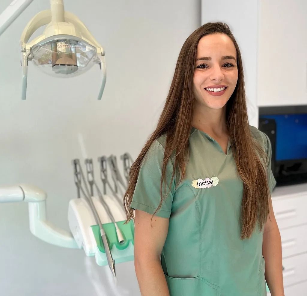 Una mujer con un uniforme verde está parada frente a un sillón dental.