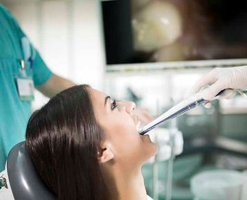 Una mujer está sentada en una silla dental mientras un dentista le examina los dientes.
