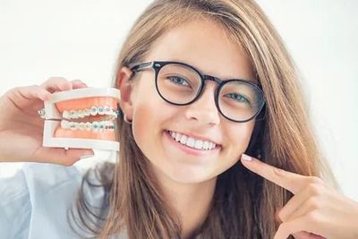 Una niña que lleva gafas sostiene un modelo de sus dientes.