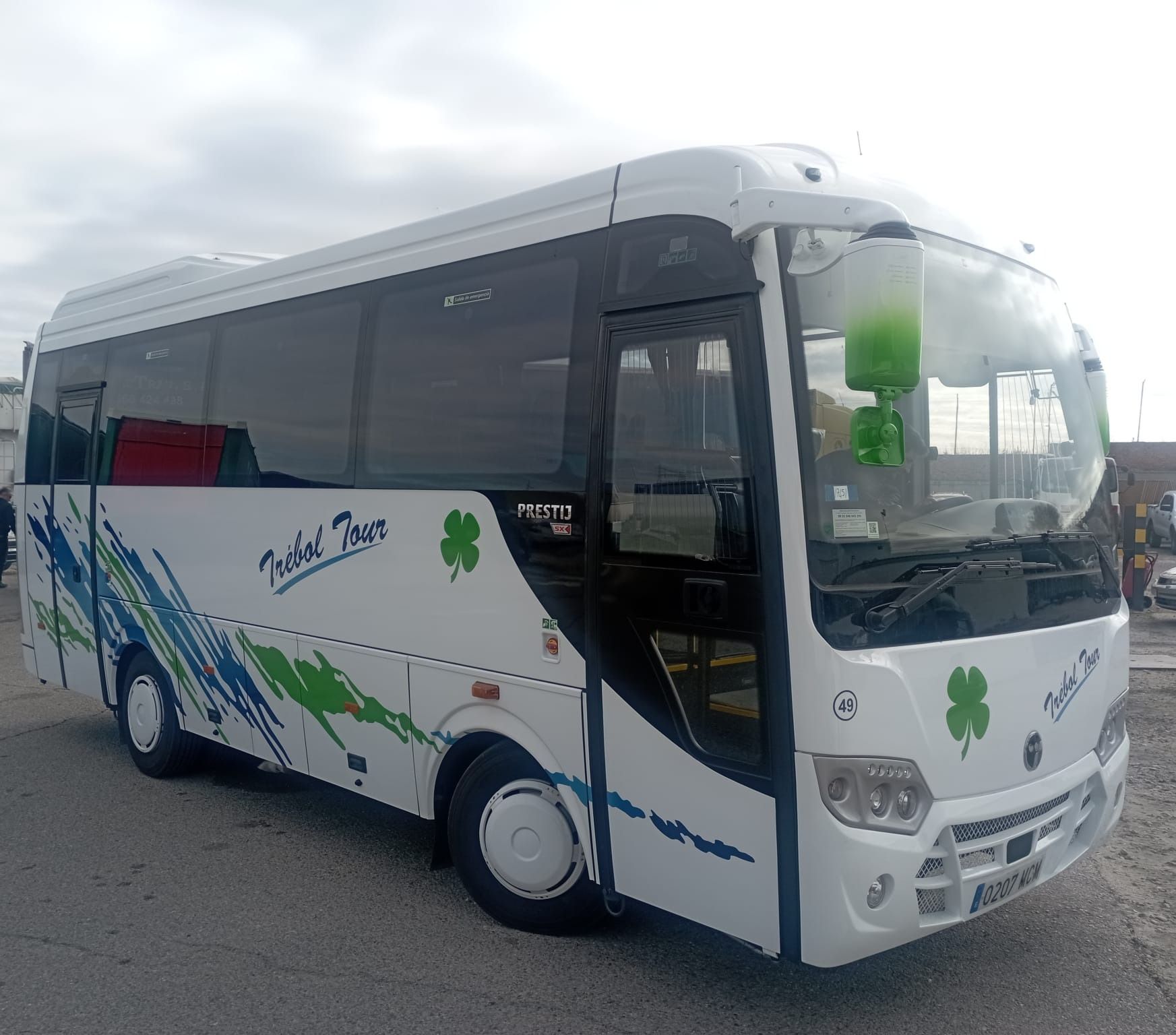 Un autobús blanco con tréboles verdes a los lados está estacionado al costado de la carretera.