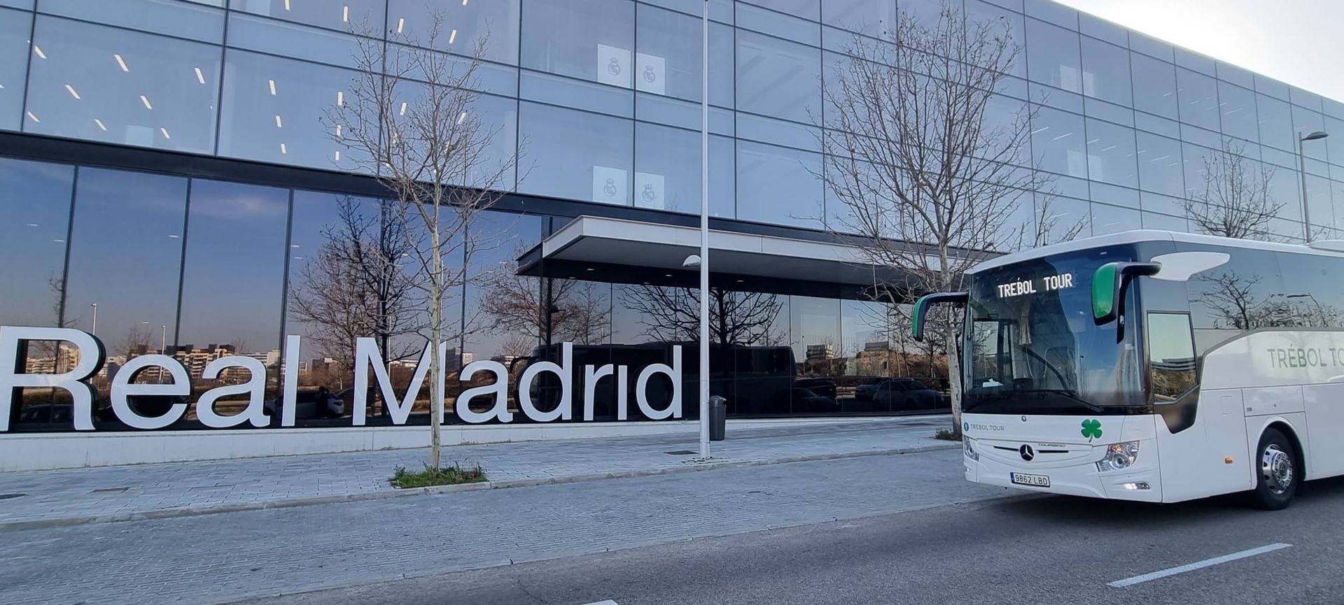 Un autobús blanco está estacionado frente a un edificio que dice Real Madrid.