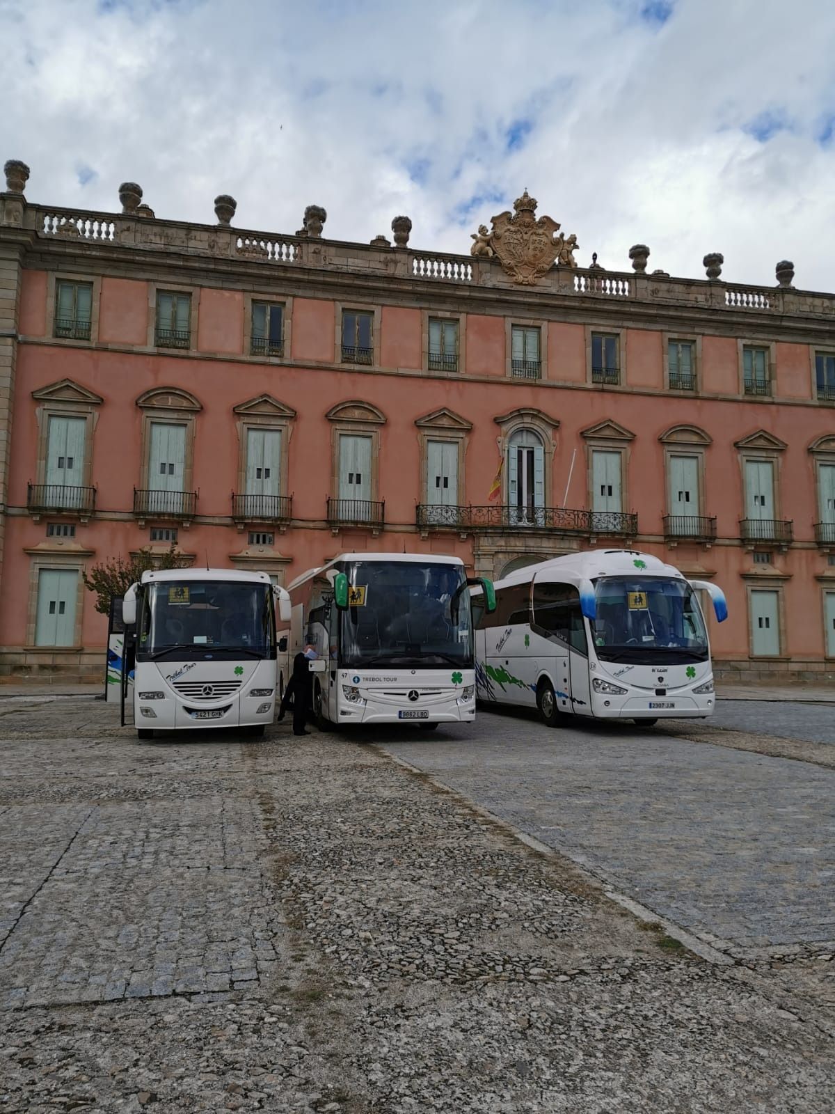 Tres autobuses están estacionados frente a un gran edificio rosa.