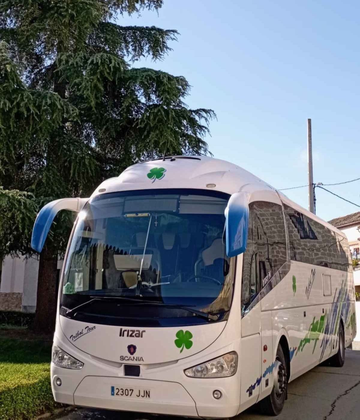 Un autobús blanco con un trébol en el frente está estacionado al costado de la carretera.