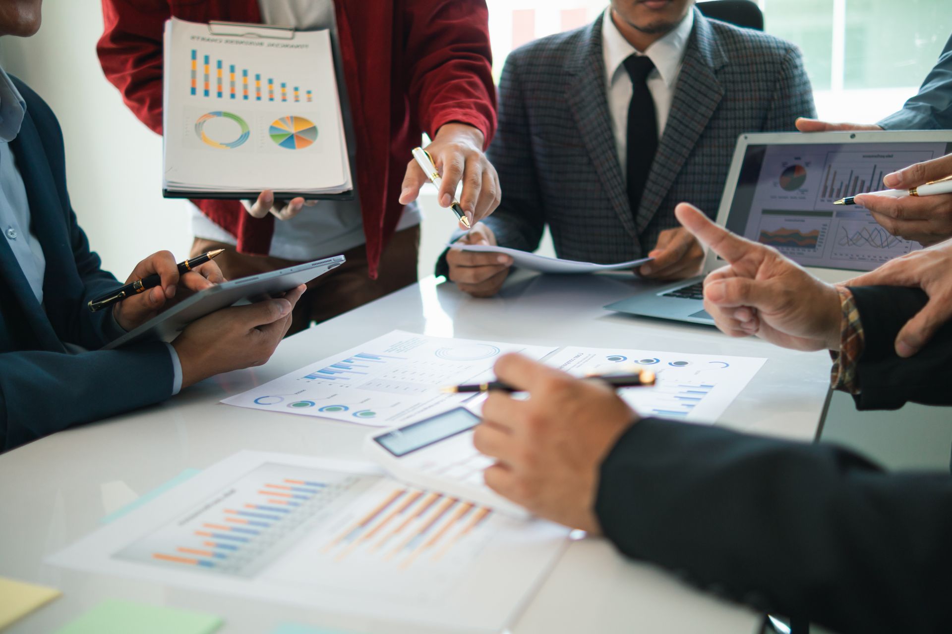 Geschäftsleute in Anzügen versammeln sich um einen Tisch, überprüfen Diagramme und Dokumente und diskutieren Geschäftsanalysen.
