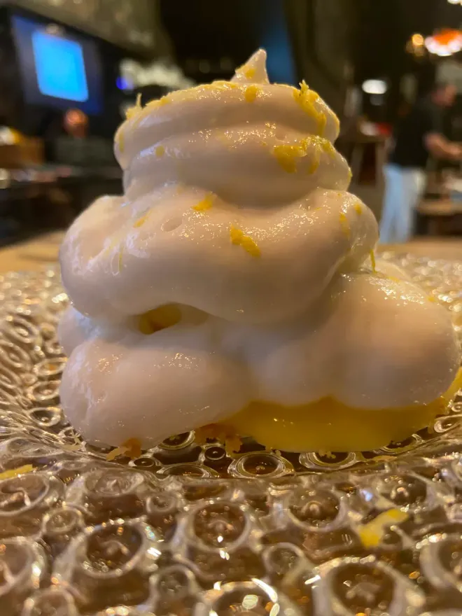 Una porción de nata montada con ralladura de naranja en un plato de vidrio texturizado, en un restaurante con poca luz