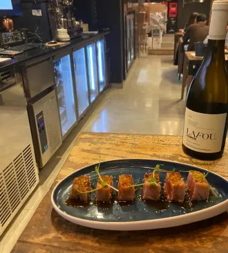 Rollos de sushi en un plato azul sobre la barra, con una botella de vino al lado.