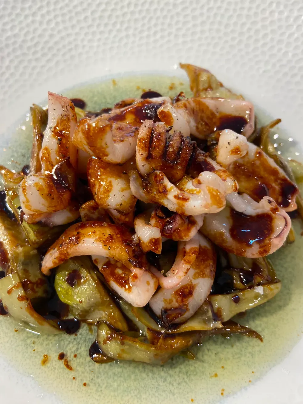 Calamares en salsa roja en un plato pequeño con guarnición verde