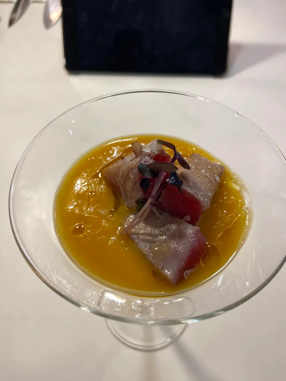 Cuenco transparente de postre con salsa de naranja y sashimi de pescado por encima, sobre una mesa blanca